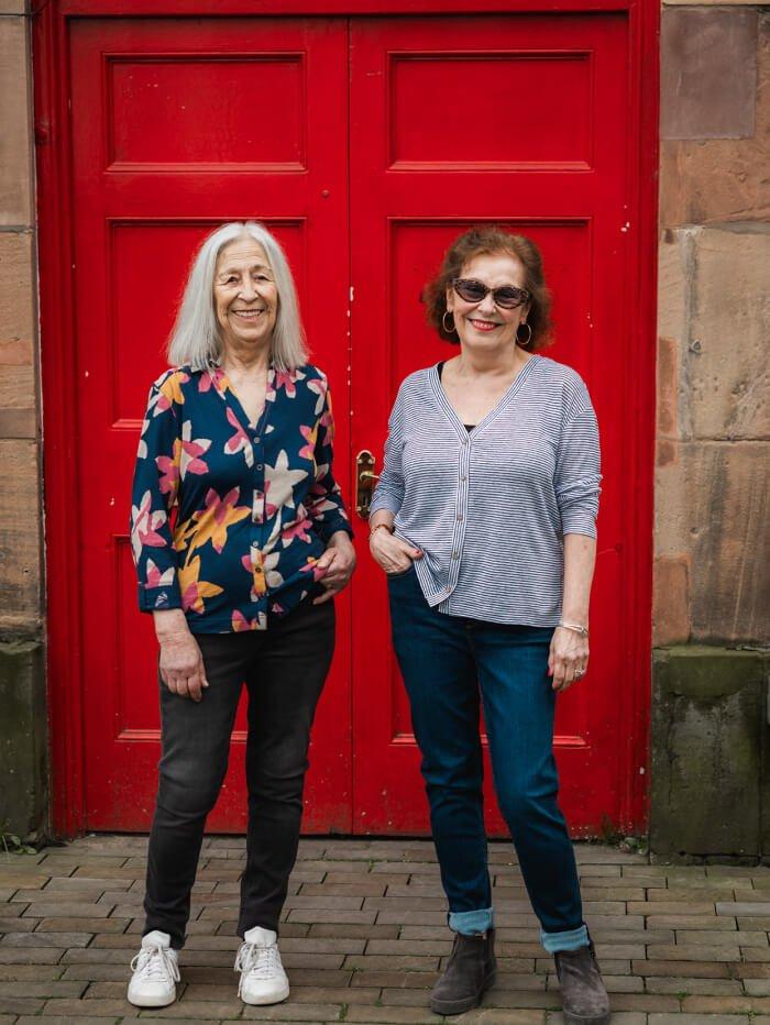 two women in jersey shirts in front of red door